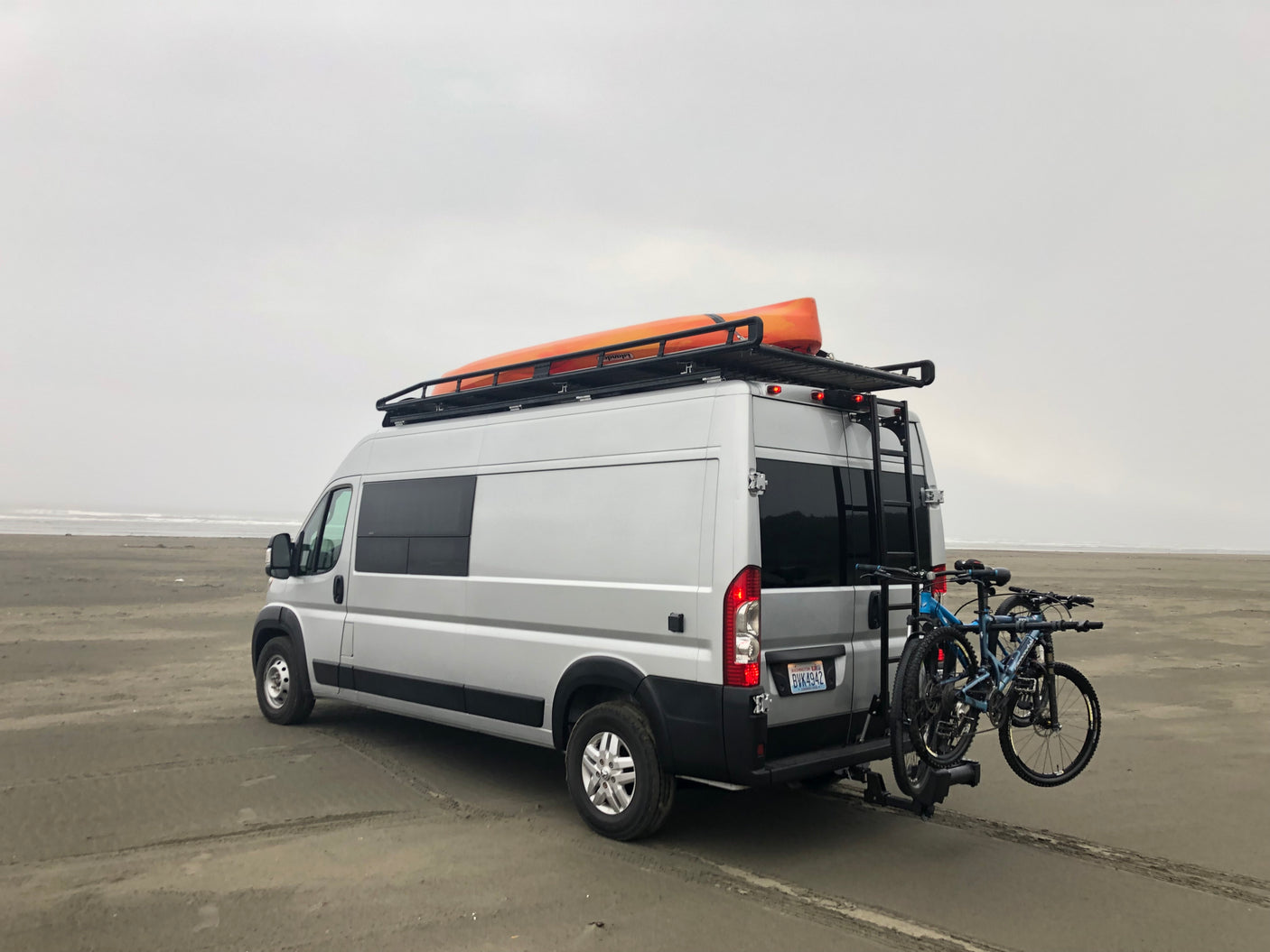This RV rental on a sandy beach features a kayak and two bikes, perfect for outdoor adventure and travel.