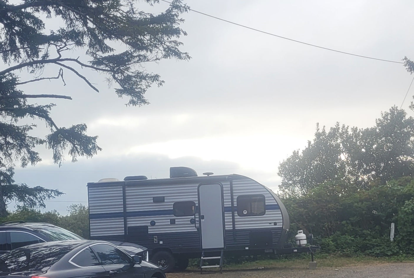 An RV rental travel trailer is parked outdoors under an overcast sky, with cars and trees nearby. Ready for camping!
