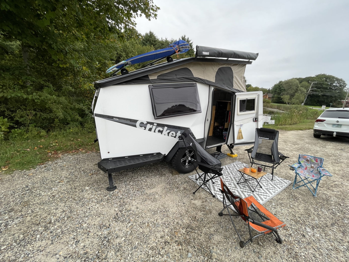 and a cozy rug by the pond.|Cozy RV rental setup by a serene lake. A compact trailer with an awning