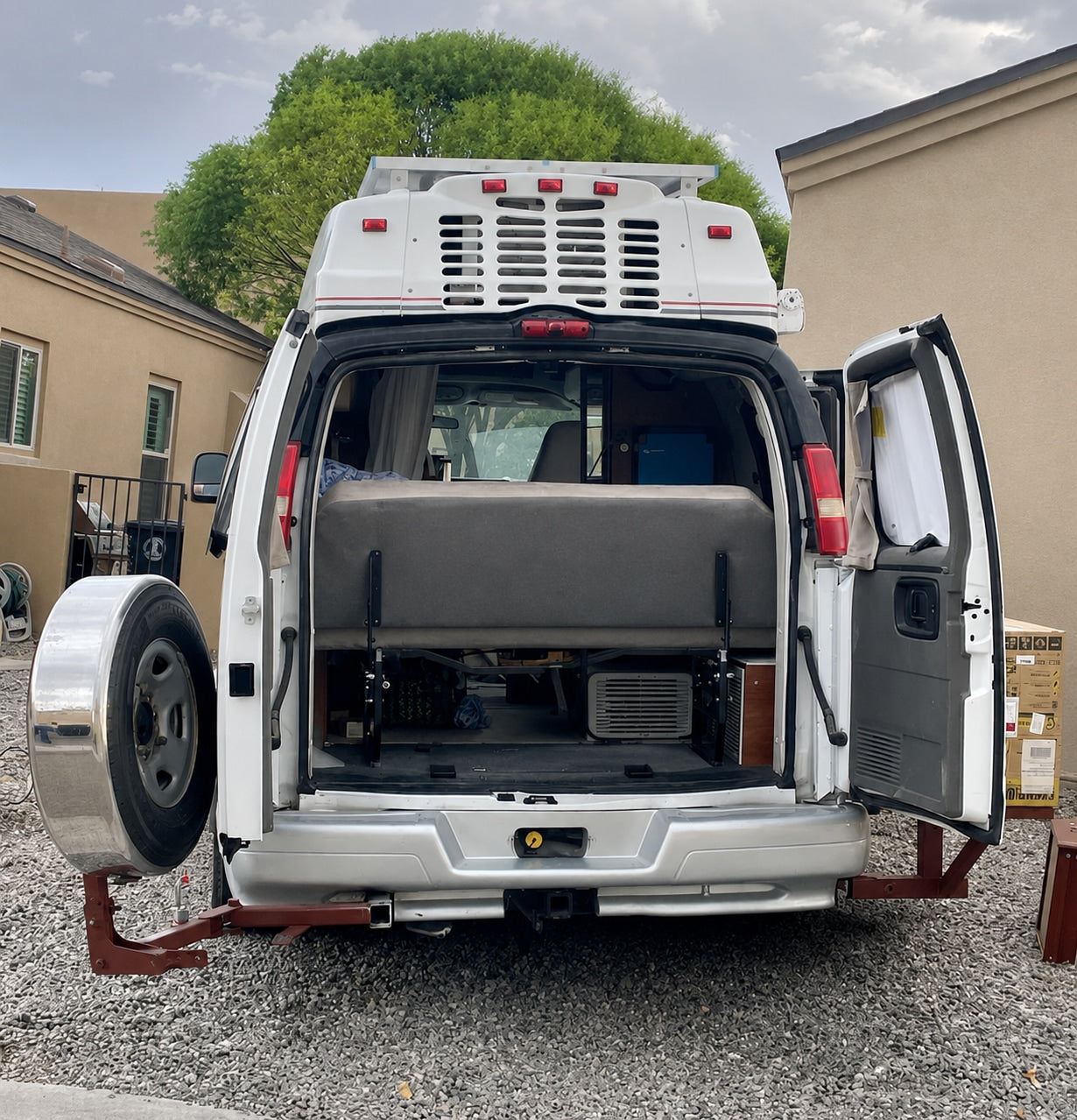 Open rear of a white camper van, ready for adventure. Features a spare tire mount, interior bed, and roof AC. Perfect for an RV rental trip.