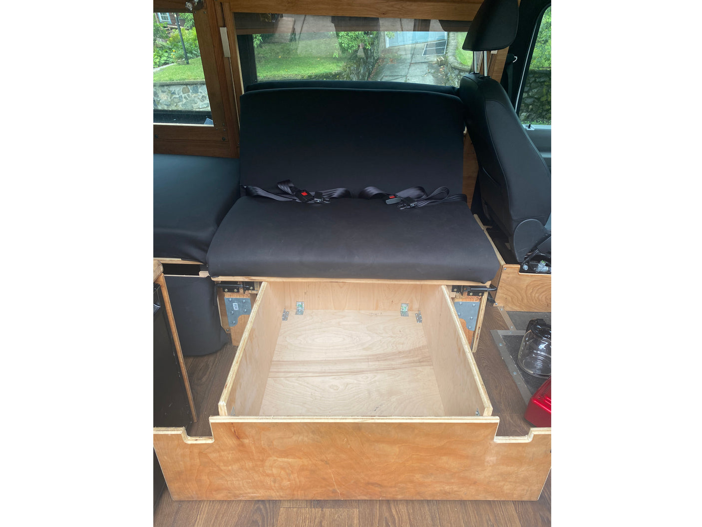 RV rental: Open wooden drawer beneath black padded seating with seatbelts, offering a glimpse of the outdoor scenery.