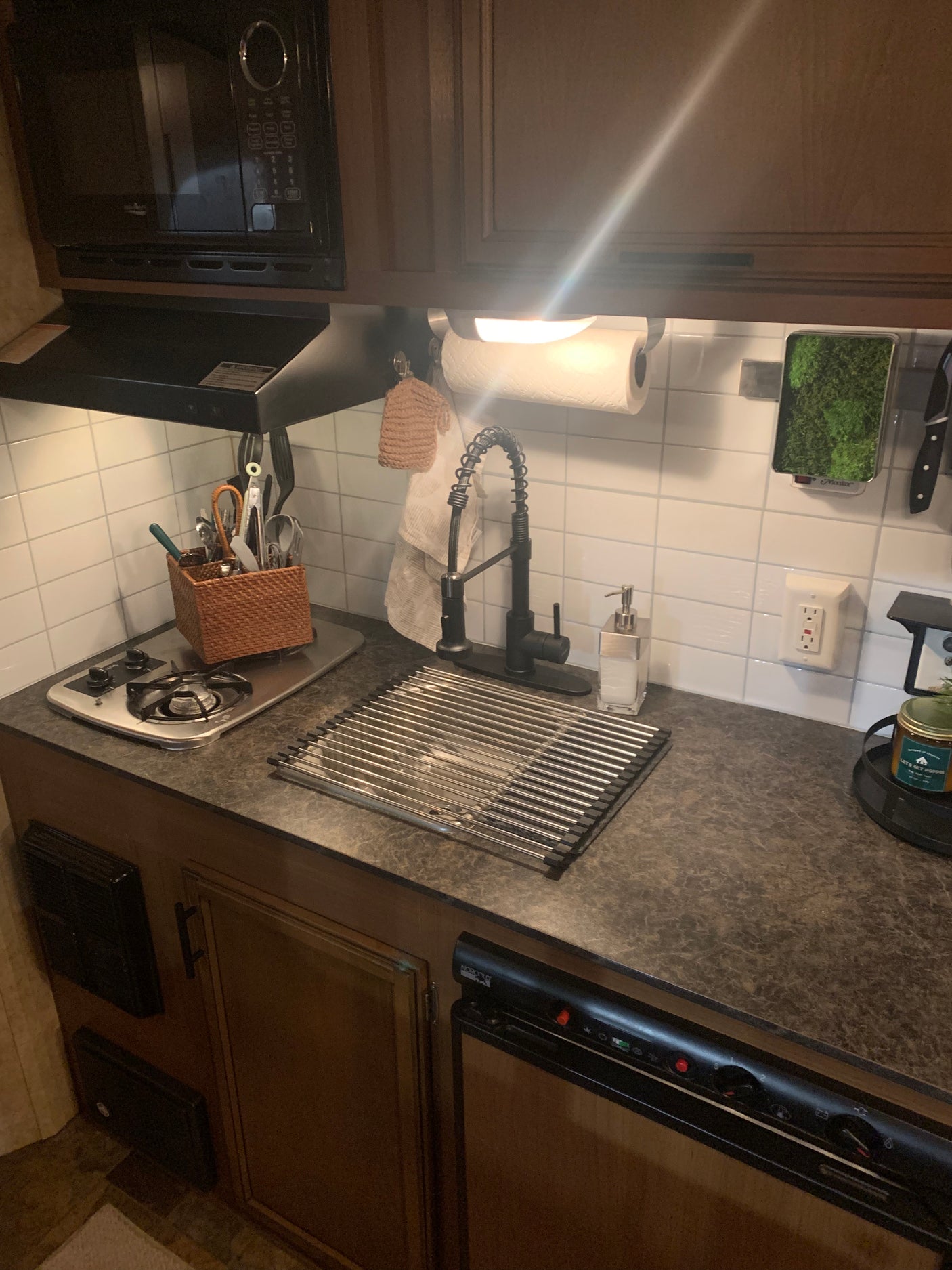 View of an RV rental kitchen: compact space with microwave, stovetop, sink, drying rack, and organized utensils.