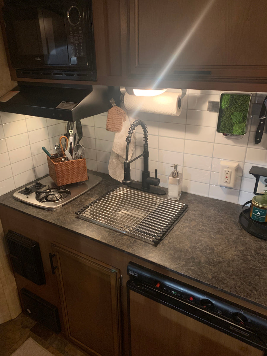 View of an RV rental kitchen: compact space with microwave, stovetop, sink, drying rack, and organized utensils.