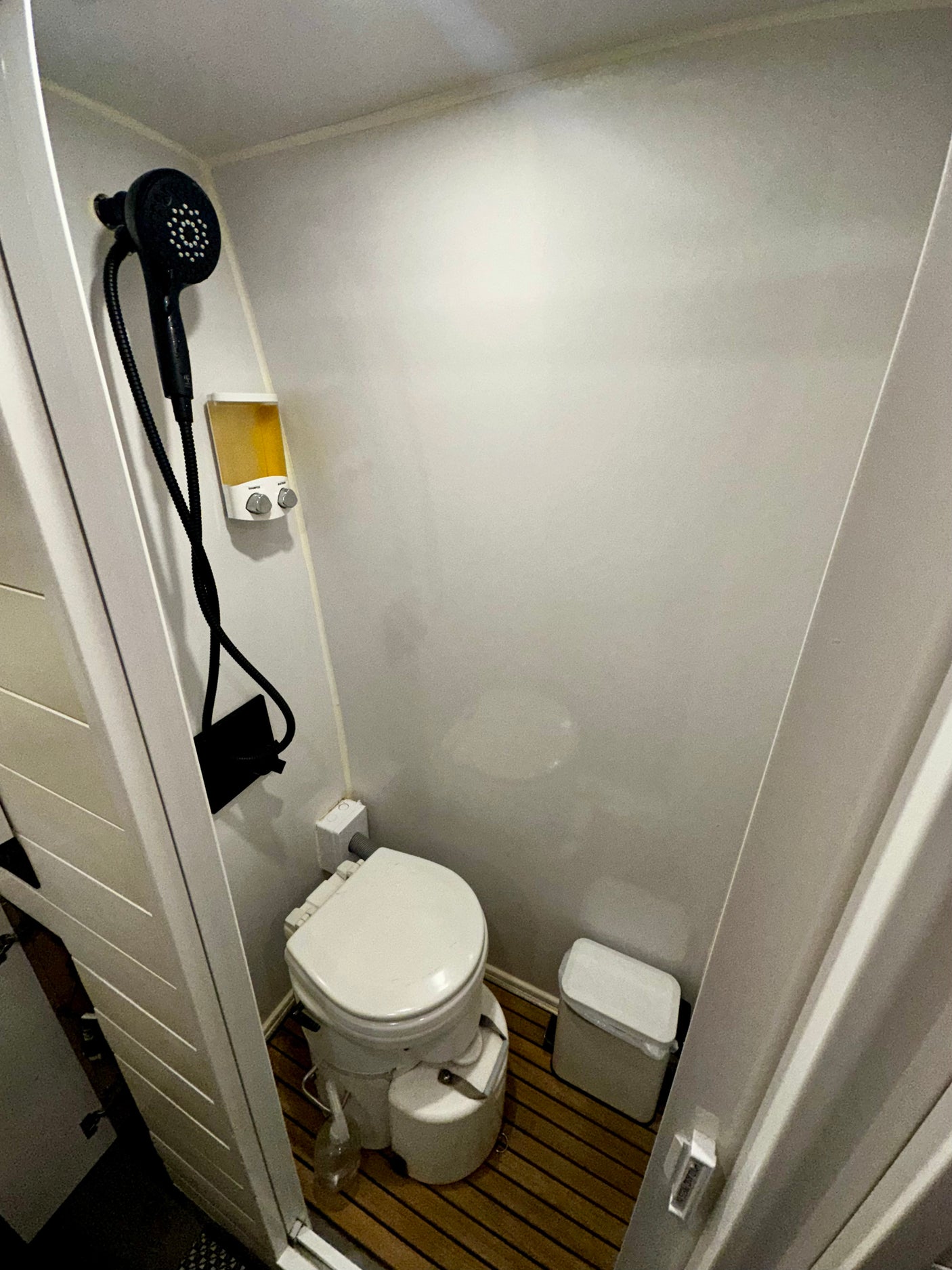 This RV rental bathroom offers a compact design with a composting toilet, shower head, and wall-mounted soap dispenser.
