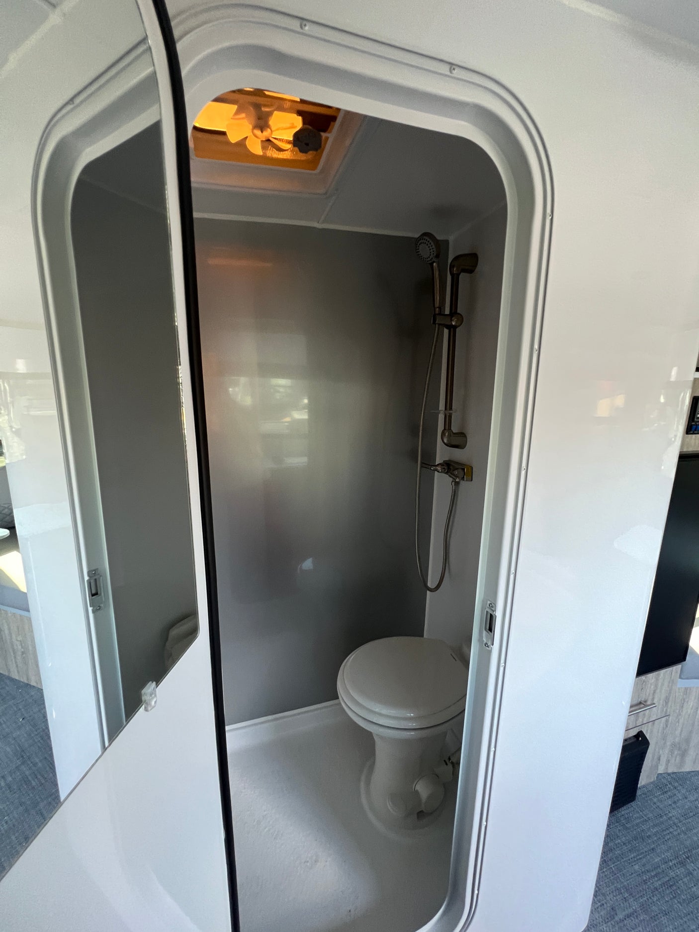 Inside a compact RV wet bath, showing the toilet, shower, and ceiling vent fan. Essential for any rv rental.