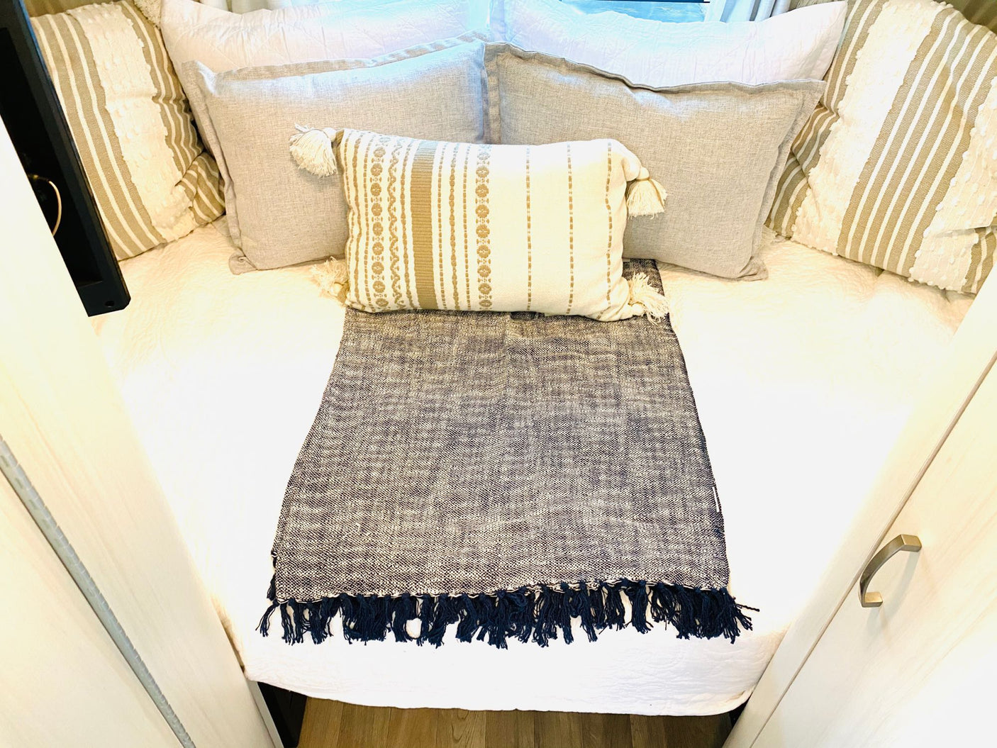 Cozy RV rental bed with neutral layered pillows, a patterned lumbar cushion, and a fringed dark throw blanket.
