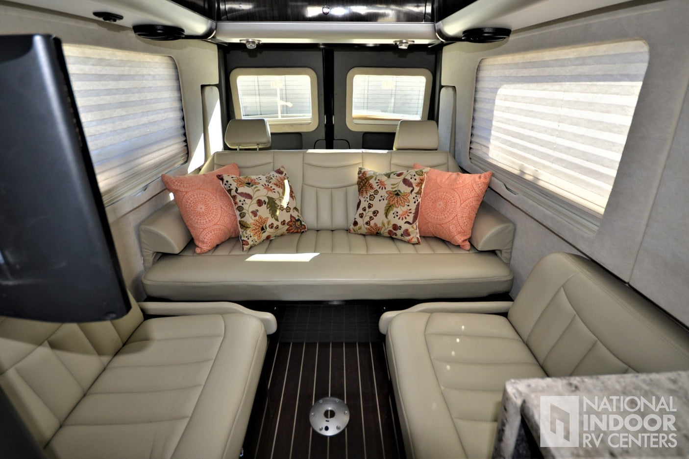 Plush RV rental interior: spacious lounge with cream sofa, decorative pillows, and facing seats on wood floor.