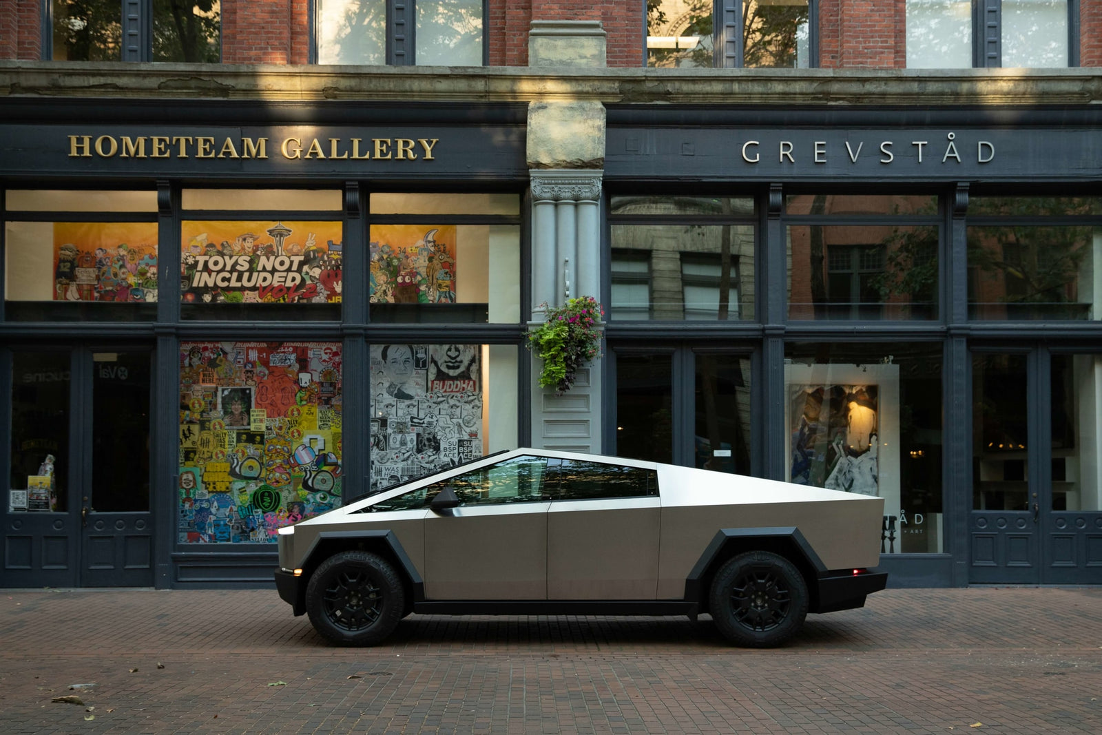 A striking Tesla Cybertruck, resembling a unique RV rental, sits on a brick street outside an art gallery. Electric adventure awaits.