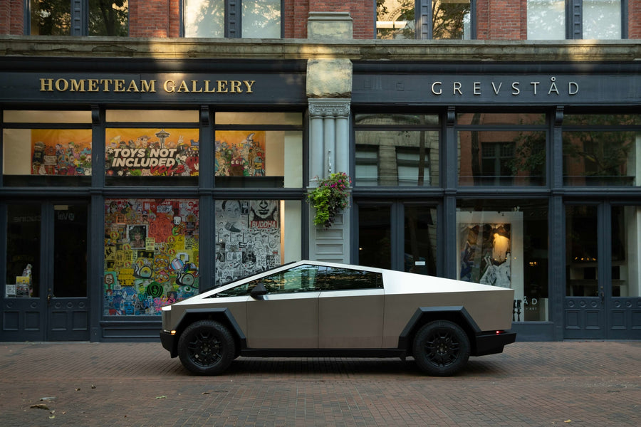 A striking Tesla Cybertruck, resembling a unique RV rental, sits on a brick street outside an art gallery. Electric adventure awaits.