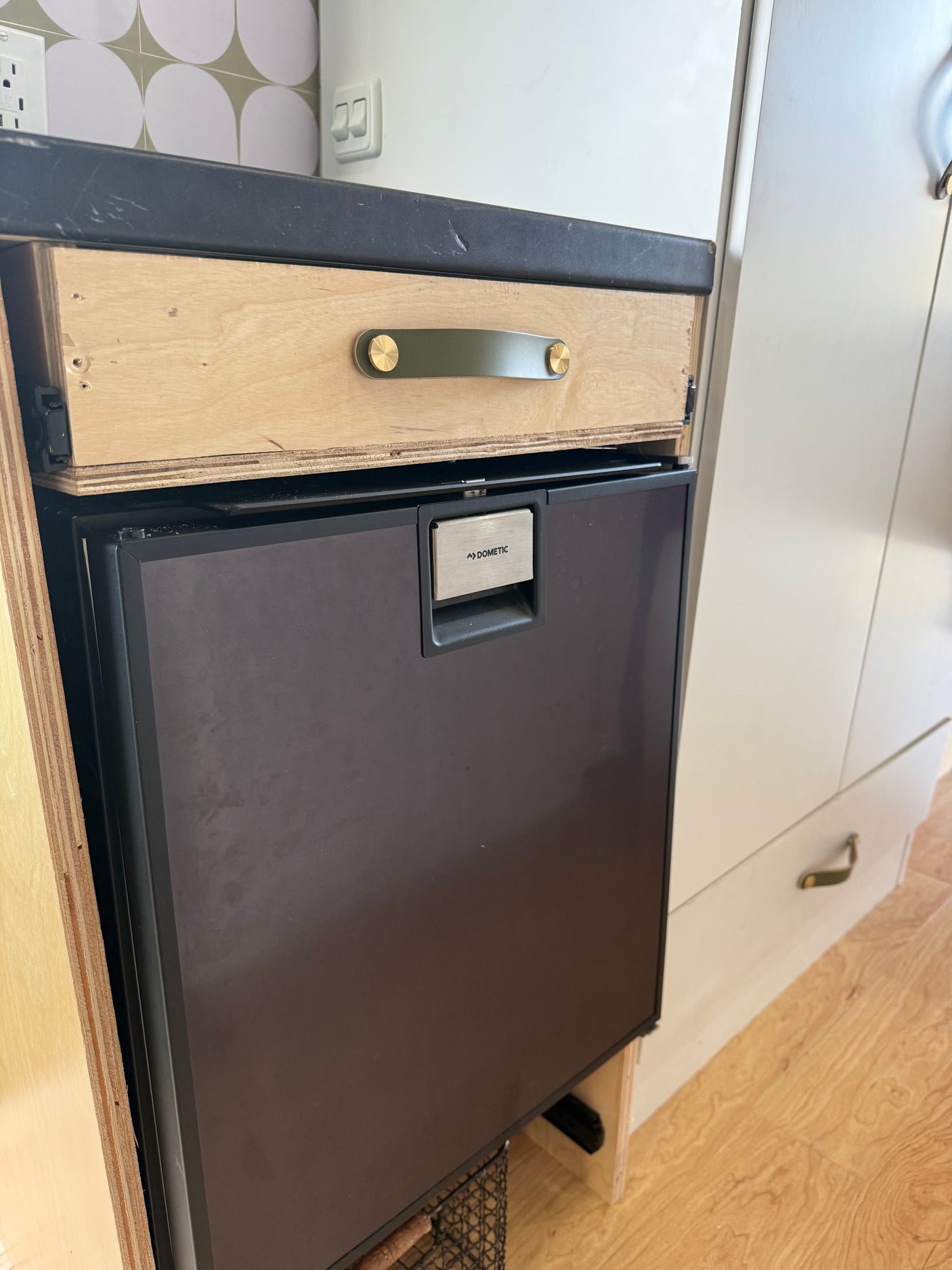 Inside this RV rental: a Dometic refrigerator, a wooden drawer with a distinctive green and brass handle, and light cabinetry.
