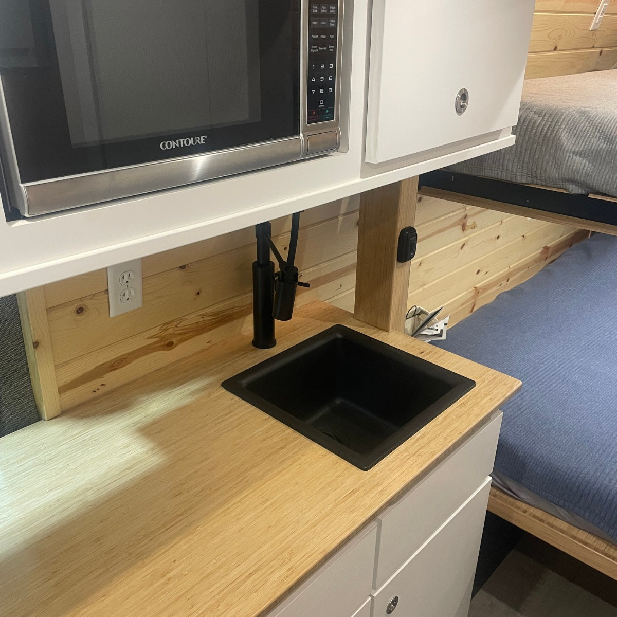 RV rental kitchen: compact microwave, black sink, wood counter, and bunk beds in the background.