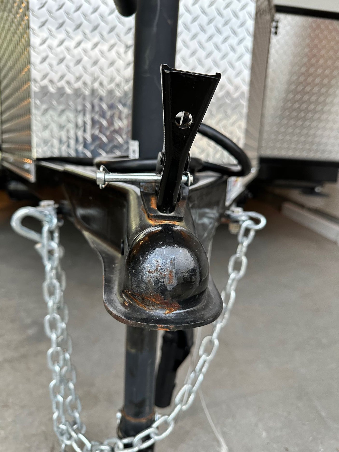 Close-up of an RV rental trailer's black hitch coupler with safety chains and a shiny diamond plate surface.