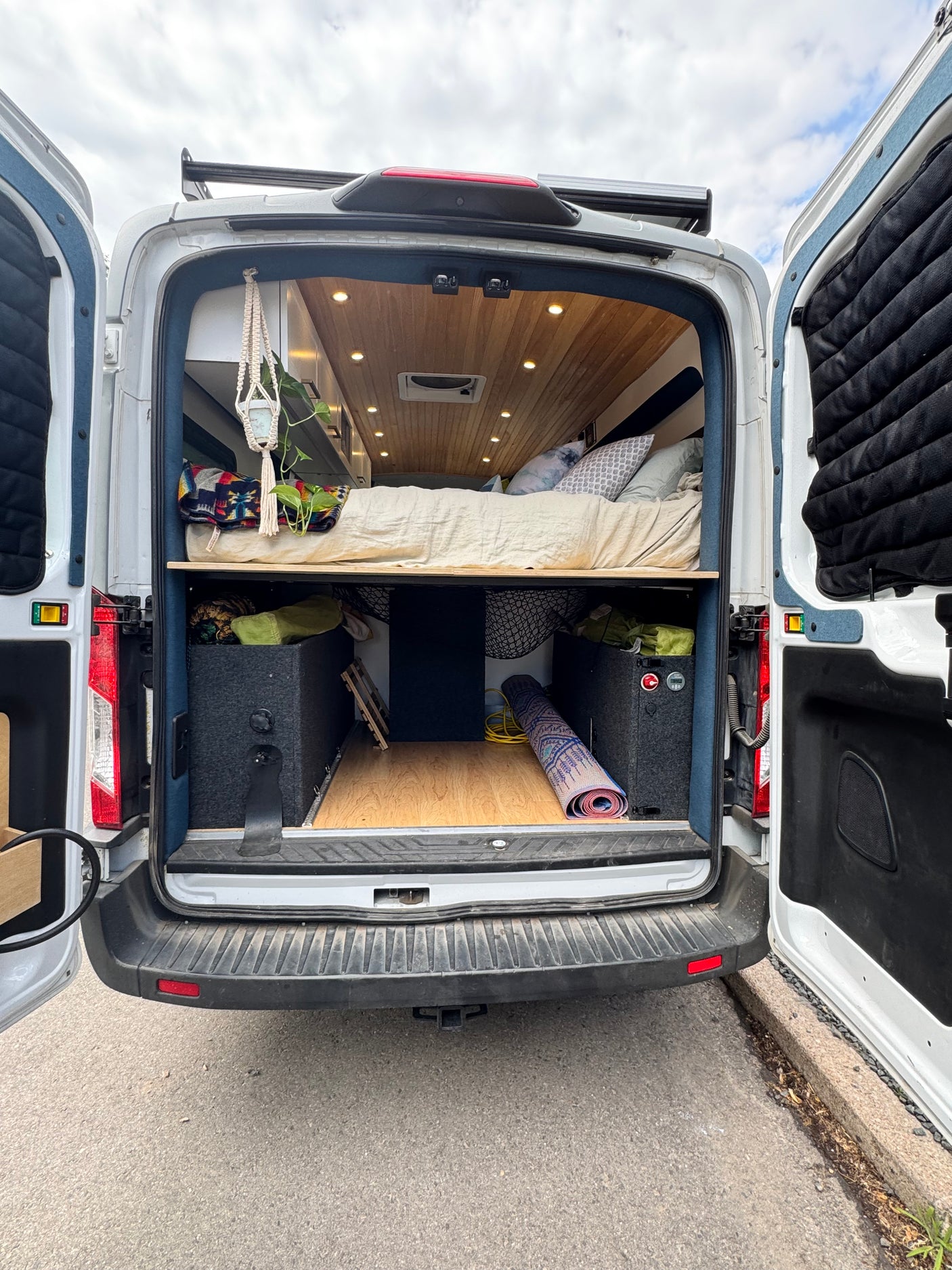 RV rental: Rear view of a customized camper van interior with bed and storage, doors open.