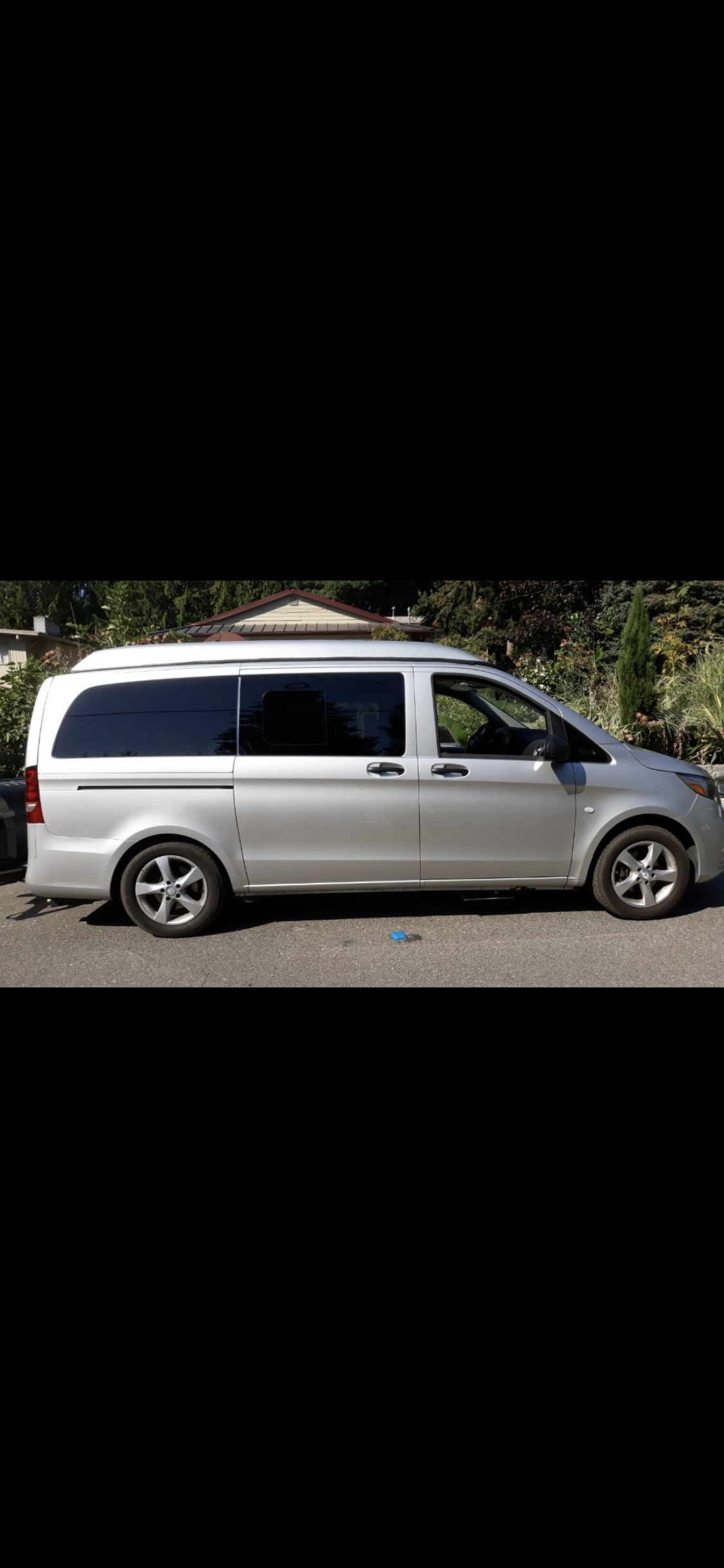 Silver Mercedes-Benz camper van for RV rental. Side profile shows tinted windows & raised roof, parked on asphalt.