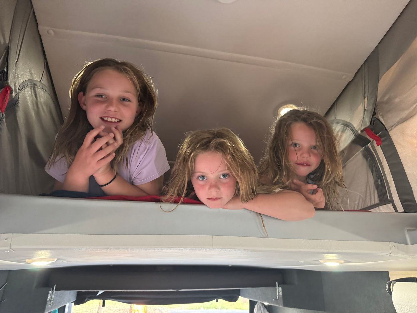 Three happy kids peek from their RV rental bunk, enjoying family travel and adventure.