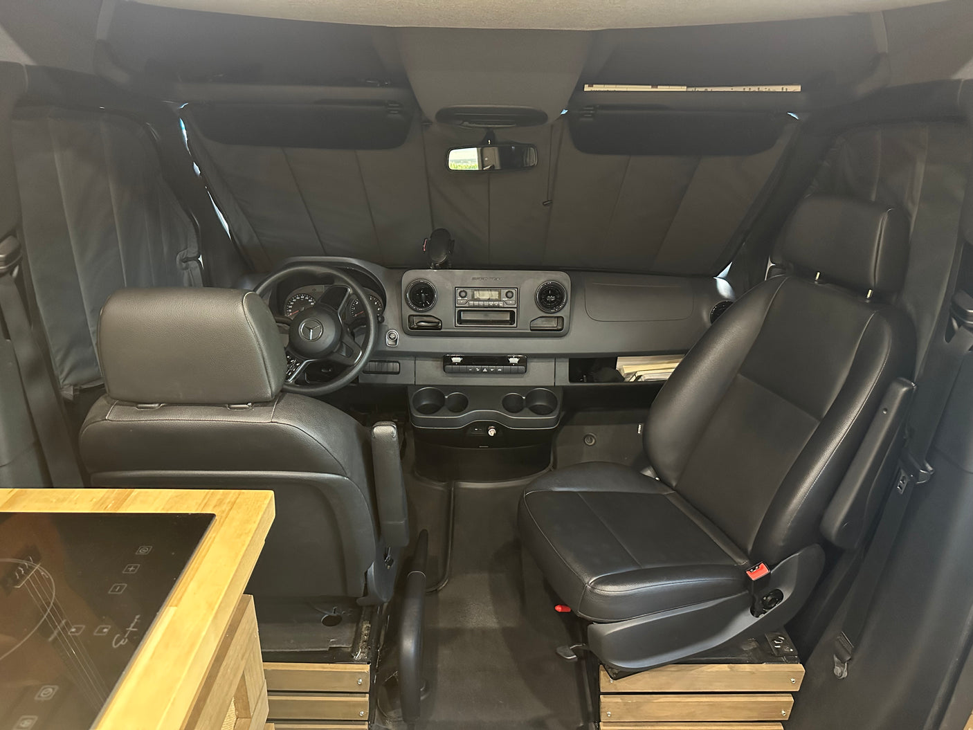 RV rental: Van interior with black seats, dashboard, and a custom cooktop, ready for your next adventure.