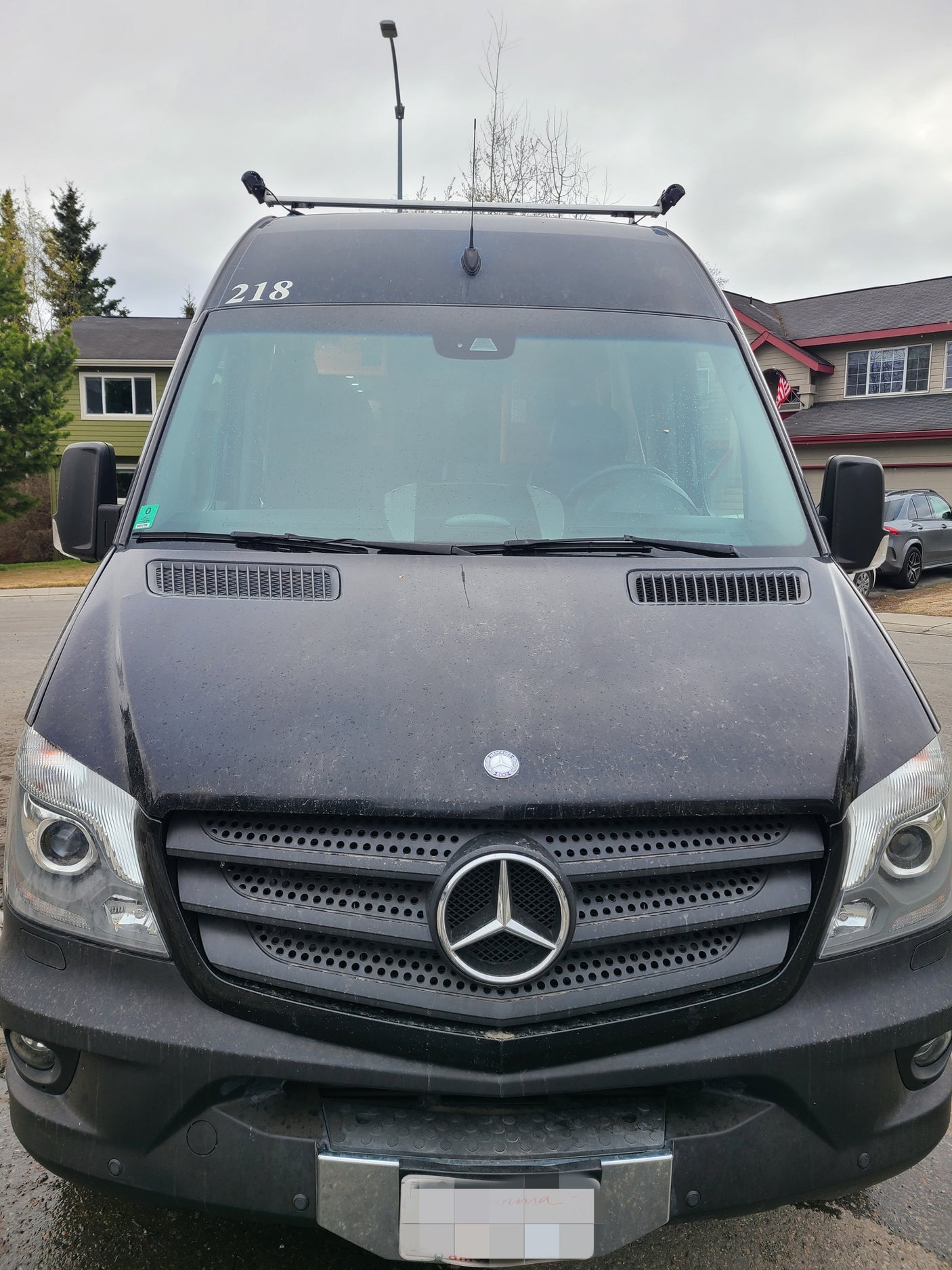 Front view of a black Mercedes-Benz Sprinter van, popular for rv rental, showing roof equipment and obscured plate.
