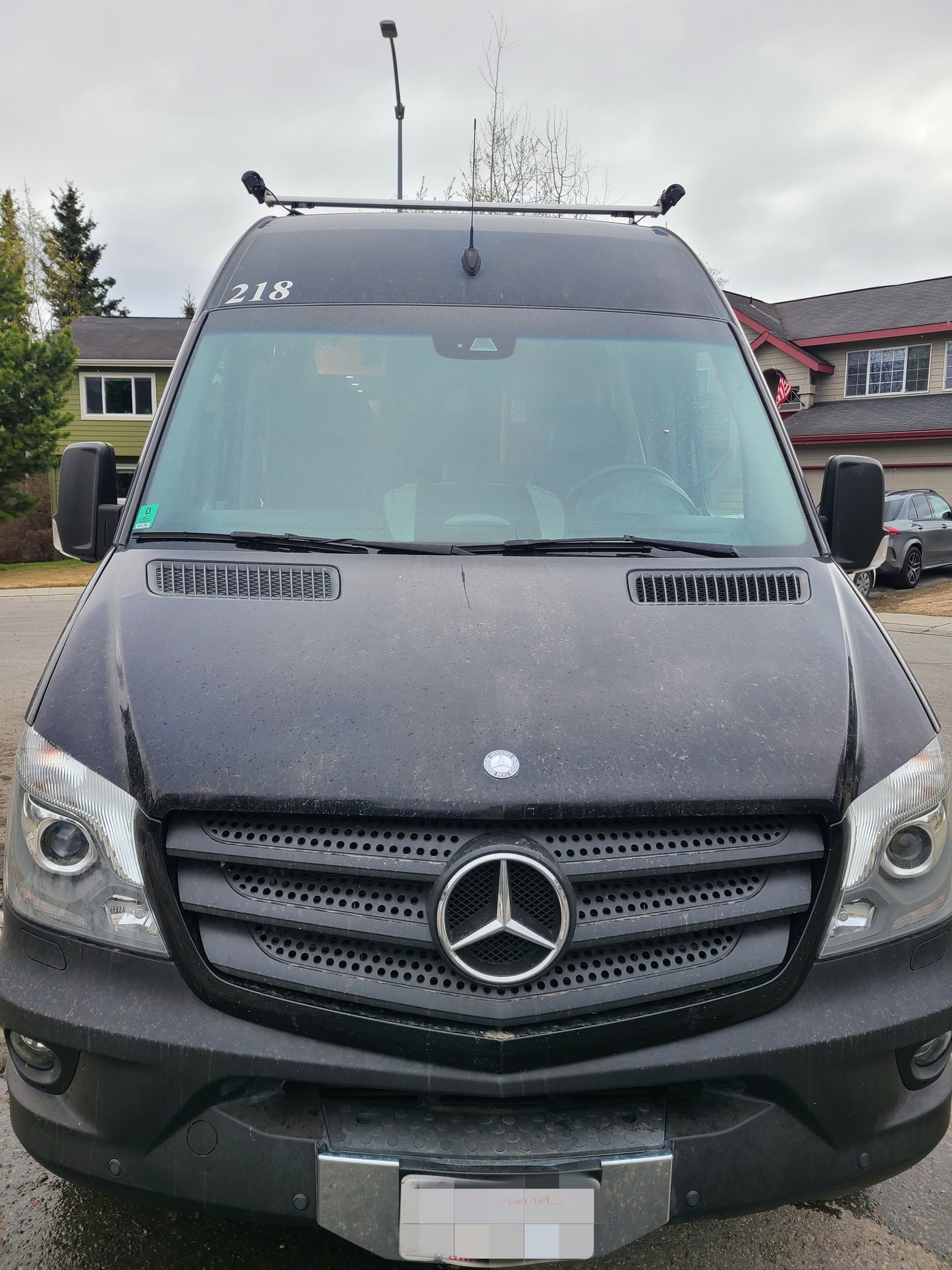 Front view of a black Mercedes-Benz Sprinter van, popular for rv rental, showing roof equipment and obscured plate.
