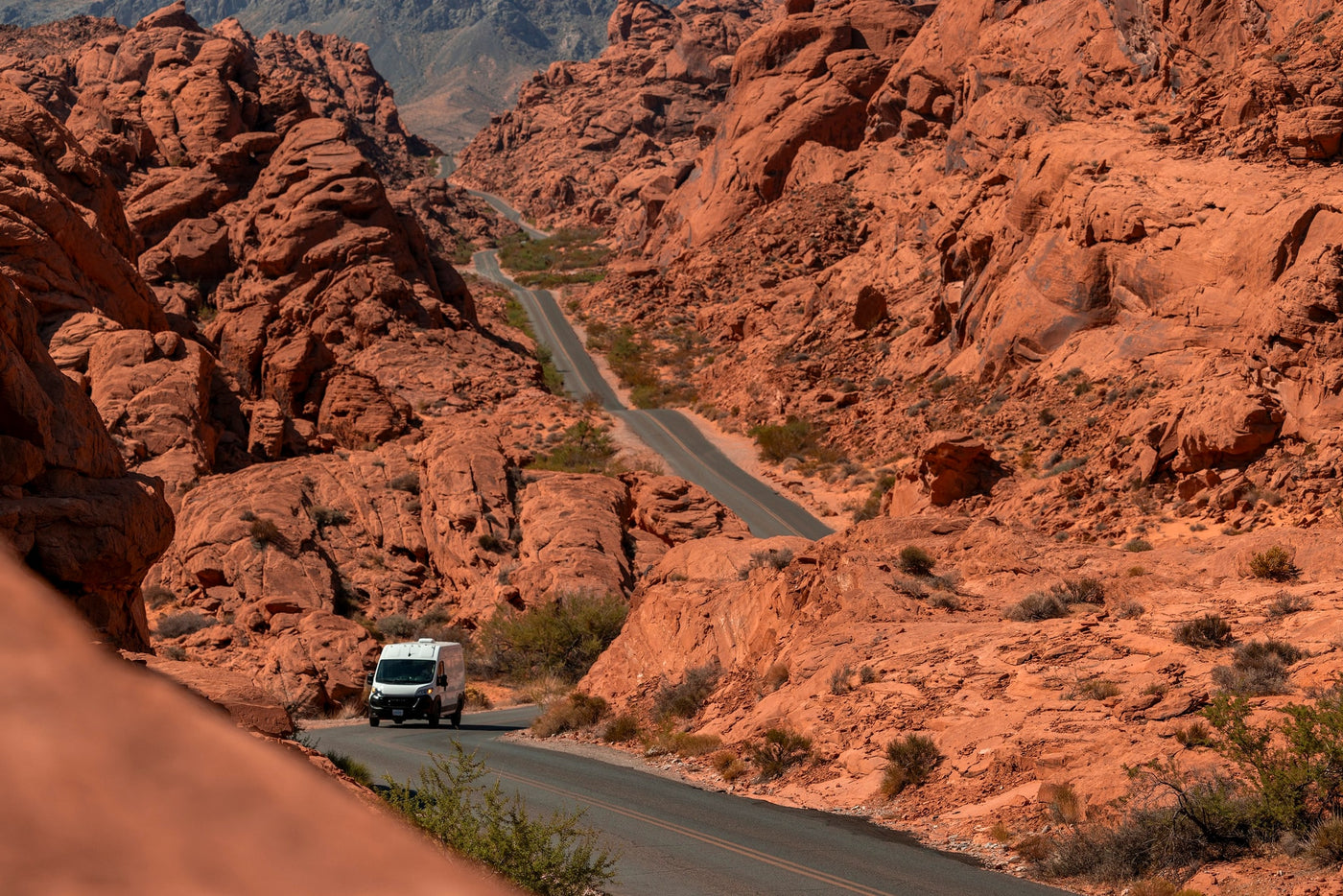 A white RV rental van on a winding road through a vast, stunning red rock canyon. — photo 2