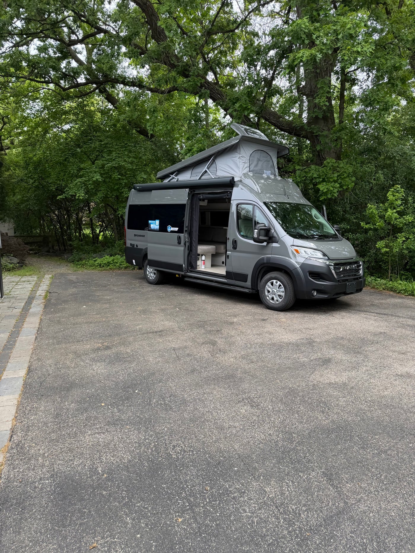 A modern gray camper van with an extended pop-top roof is parked on asphalt, ready for your rv rental adventure amidst lush trees. — photo 14