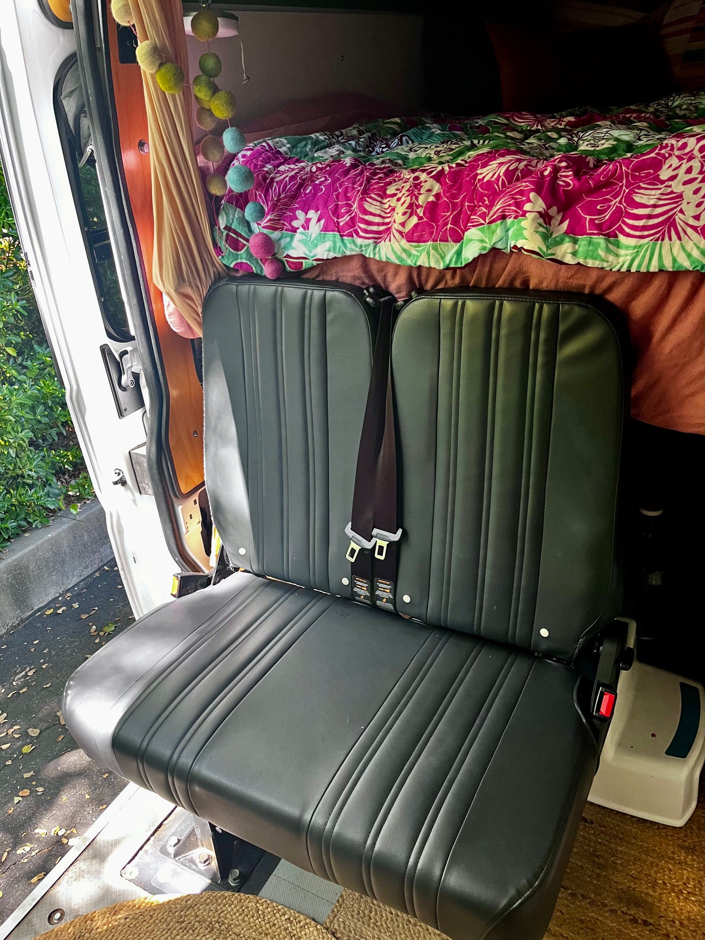RV rental interior: black seats with belts, colorful bed, and charming decor. Ideal for van life travels.