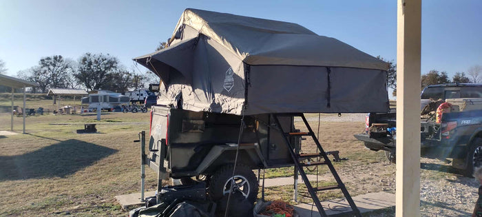 a robust RV rental alternative for outdoor trips.|This RV rental setup features a unique rooftop tent on an off-road trailer at a sunny campsite. Ideal for overlanding & camping.|This mobile RV rental offers lakeside camping with an open rooftop tent and a self-contained kitchen. Enjoy nature!|This unique RV rental