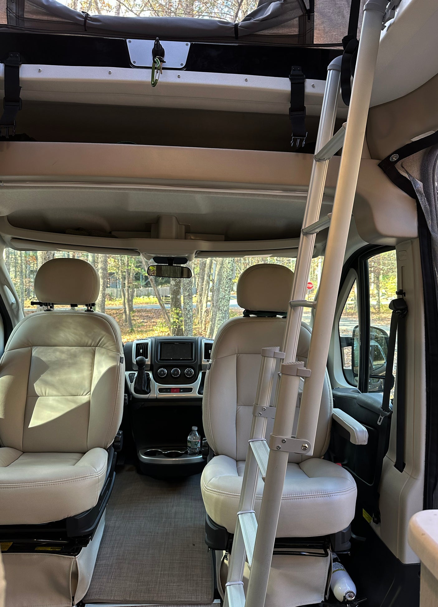 Inside an RV rental, showing the driver's cabin with front seats, dashboard, and an overhead bunk ladder.