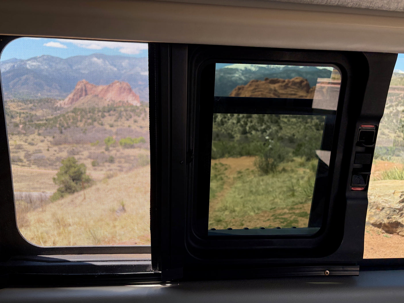 Scenic desert view from an RV rental window, with mountains and red rocks through the screen & glass. Perfect for travel!