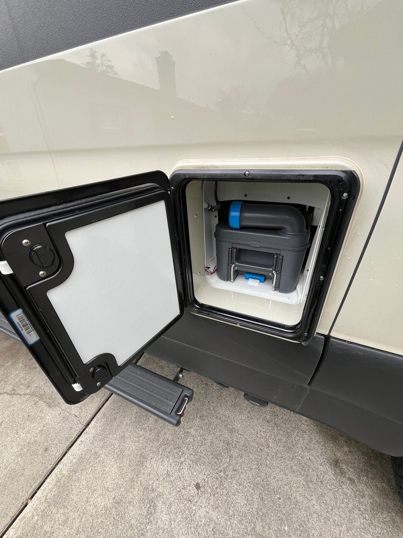 RV rental: Exterior hatch open on a cream van, revealing a grey/blue portable toilet cassette for waste disposal.