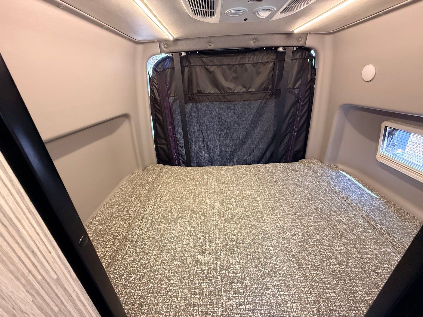 Interior of an rv rental featuring a textured bed, overhead lights, and a rear window privacy cover. Ideal for compact travel living.