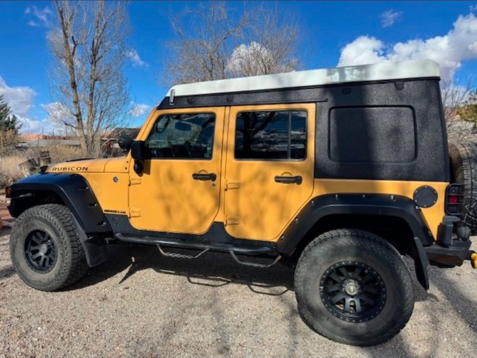 perfect for a desert adventure.|A rugged yellow Jeep Wrangler with a black overland camper top and white pop-up roof