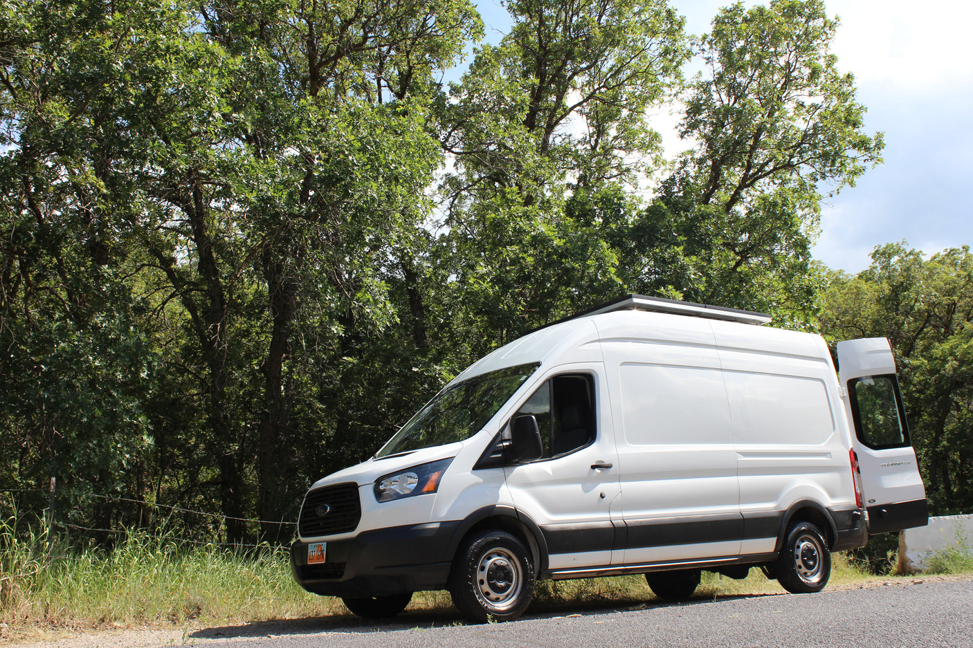 White camper van parked roadside by green trees. This RV rental is ready for scenic road trips and outdoor adventures.