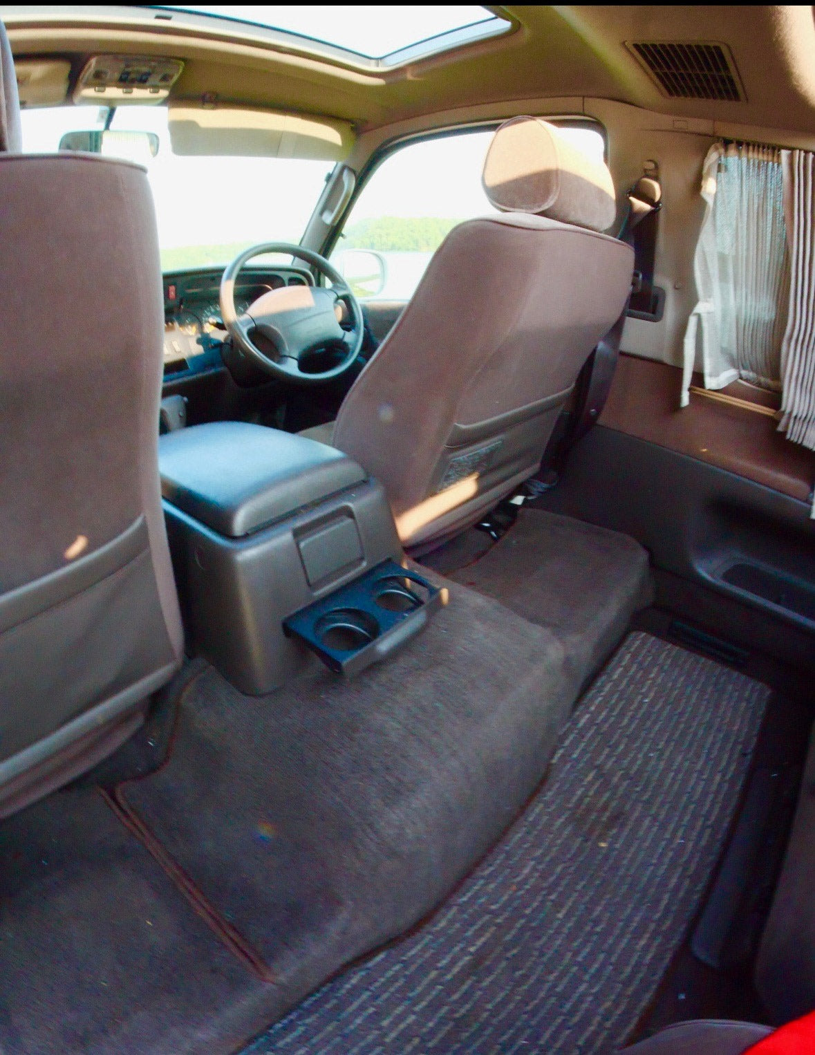 Inside this cozy RV rental: View from the back shows front seats, steering wheel, sunroof, and rear curtains for privacy.
