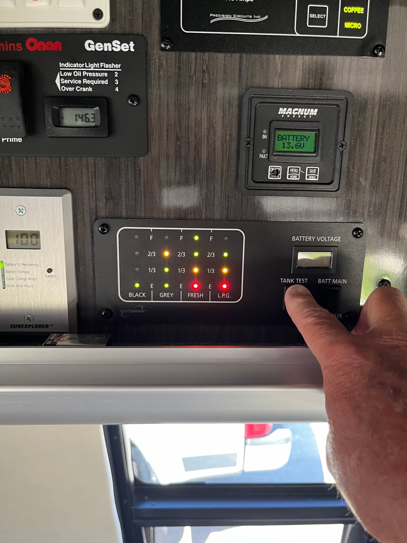 Monitoring an RV rental's systems: A hand presses a tank test button on a control panel displaying battery voltage (13.6V), generator hours (146.3), and tank levels.