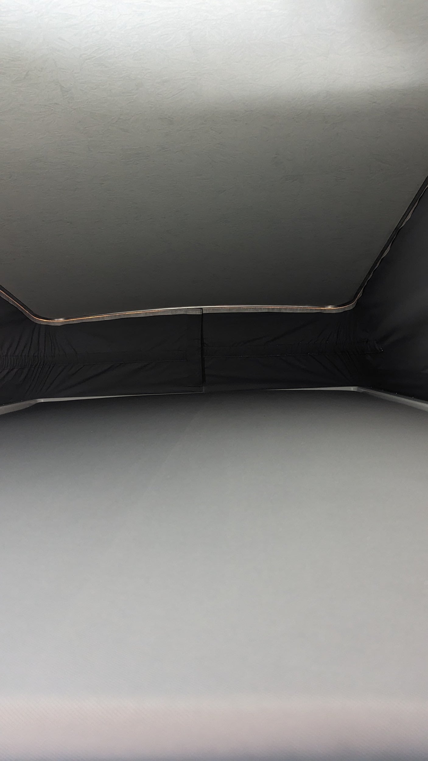 RV rental pop-top view: Raised ceiling, dark fabric walls, and mattress inside a campervan for comfortable travel.
