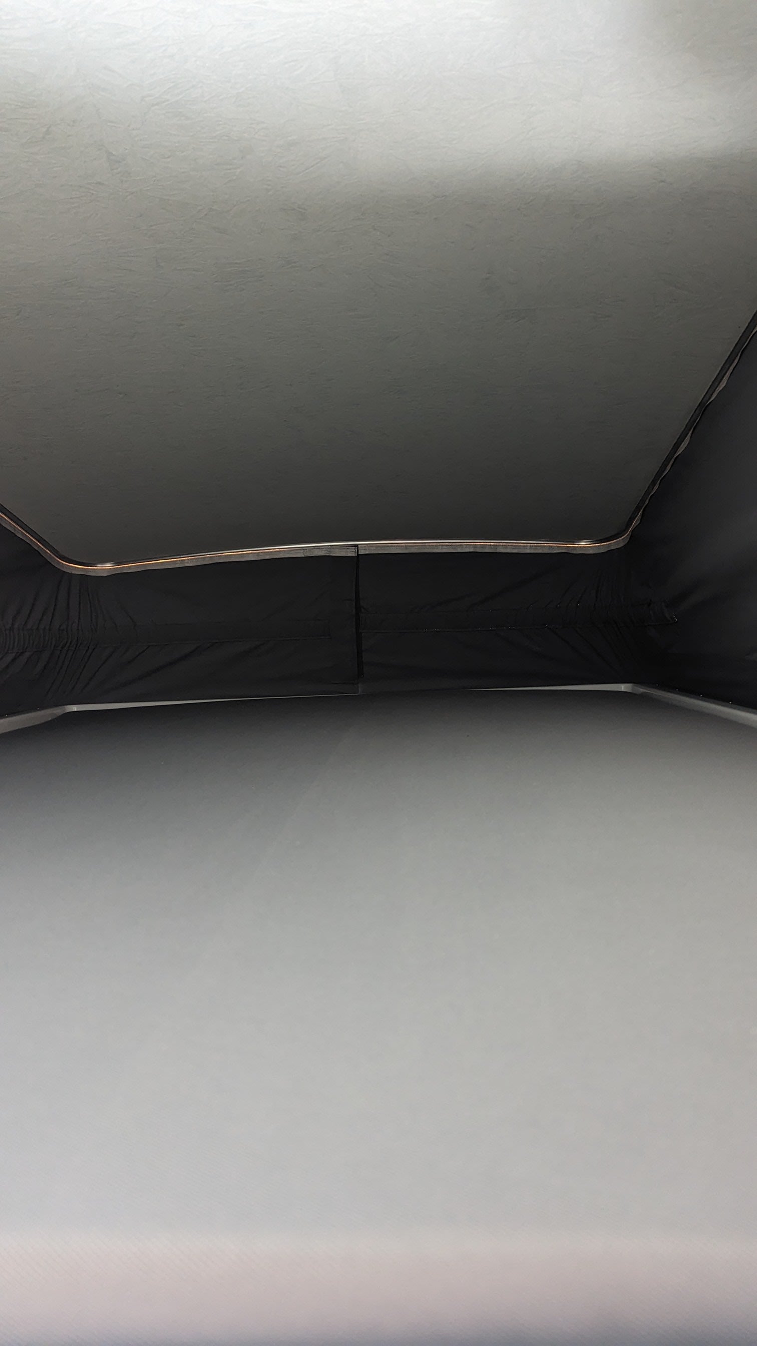 RV rental pop-top view: Raised ceiling, dark fabric walls, and mattress inside a campervan for comfortable travel.