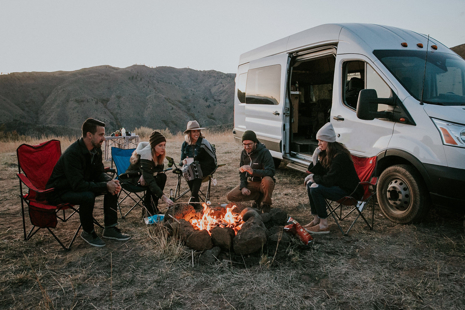 Friends enjoy a cozy campfire with s'mores alongside their RV rental, perfect for a scenic van life adventure.
