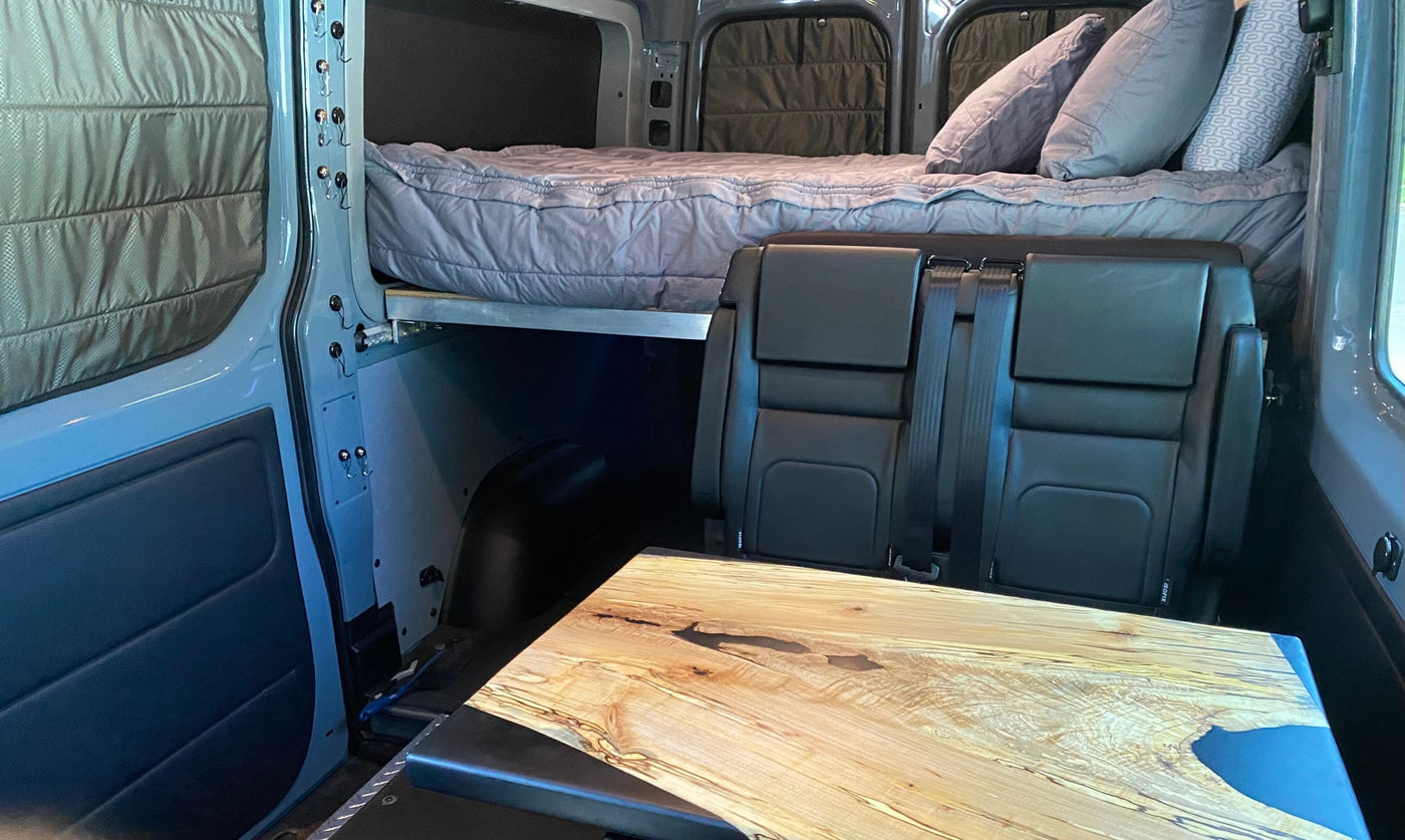 Cozy RV rental interior: elevated bed, passenger seats, and unique wooden table with quilted window coverings. — photo 12