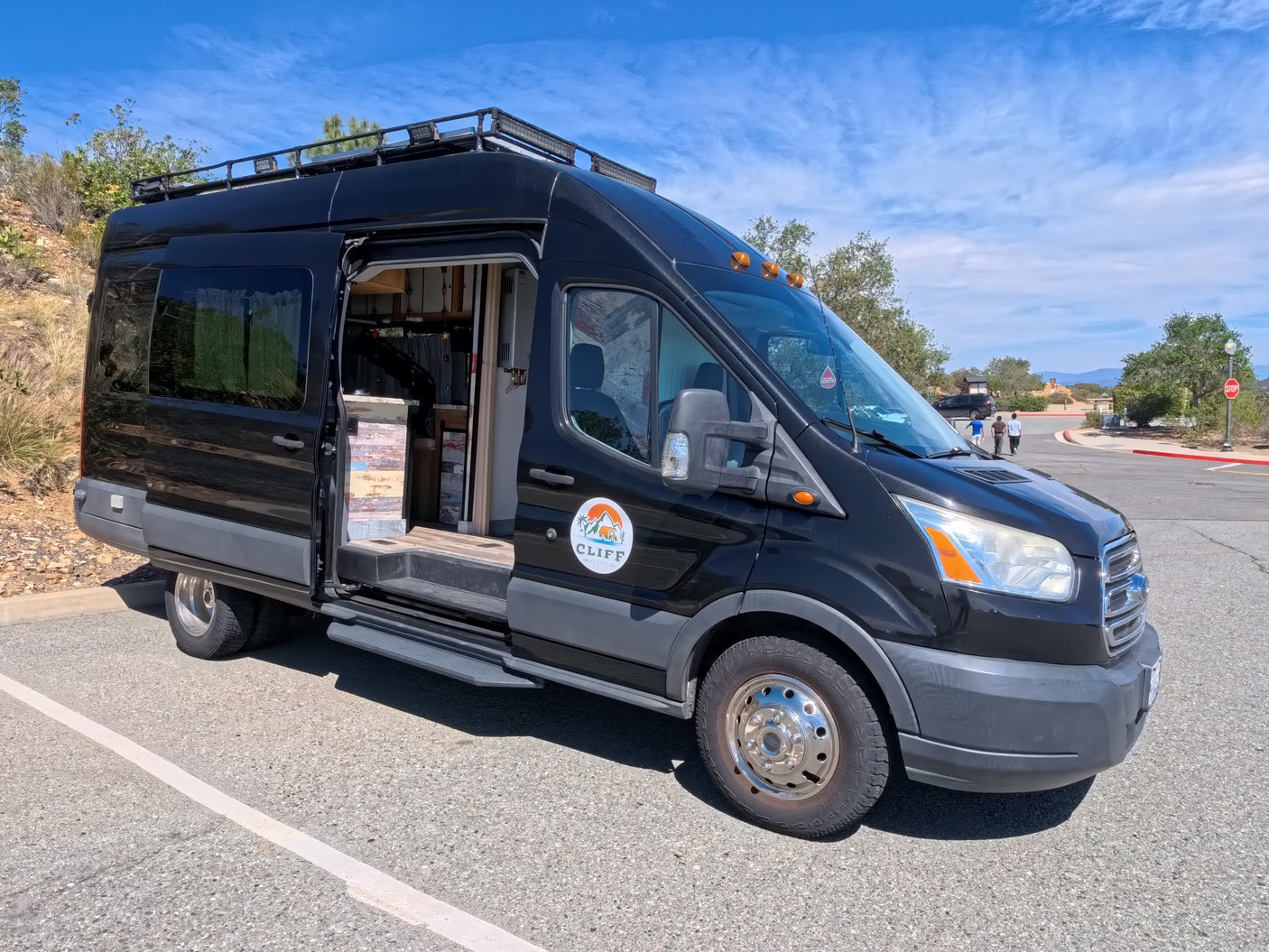 CLIFF RV rental: a black Ford Transit camper van with custom interior shown through its open side door, parked outdoors.
