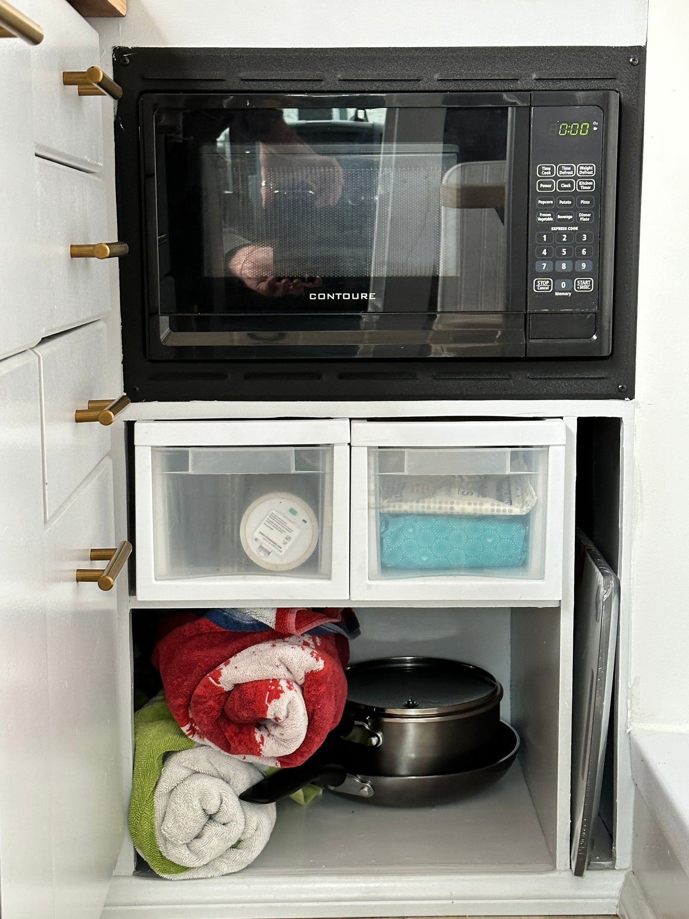 Compact RV rental kitchen: Contoure microwave, organized storage drawers, pots, pans, and towels, ready for travel.
