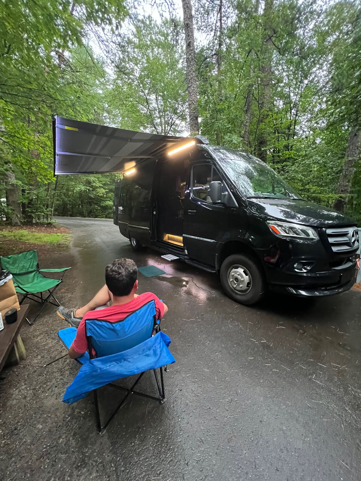 and a compact kitchen counter featuring a stovetop.|Black Mercedes-Benz Sprinter rv rental van with extended awning & open door