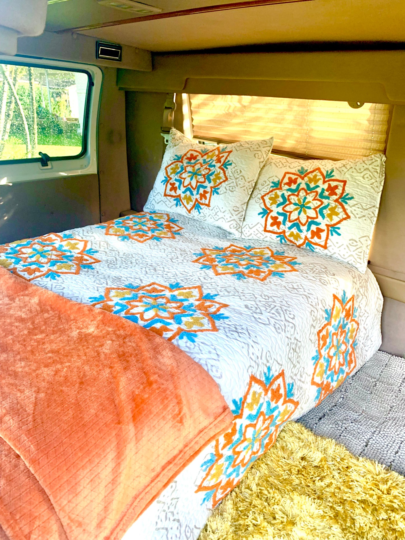 Cozy RV rental interior with a comfy bed, white and colorful mandala bedding, and a scenic window view.