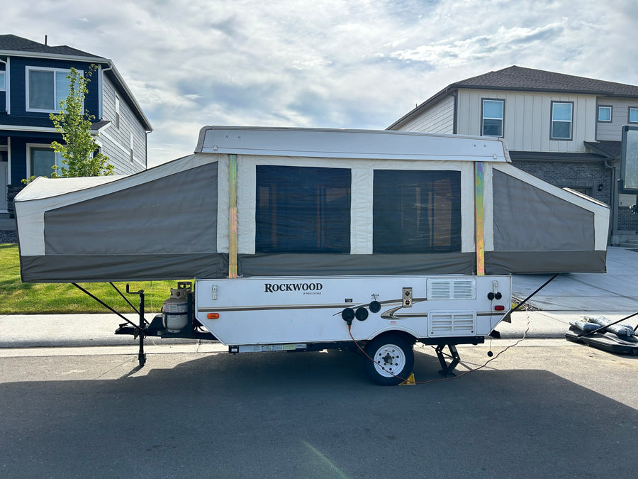 A Rockwood pop-up RV rental, fully set up with canvas sides, is parked on a street. Perfect for camping adventures.