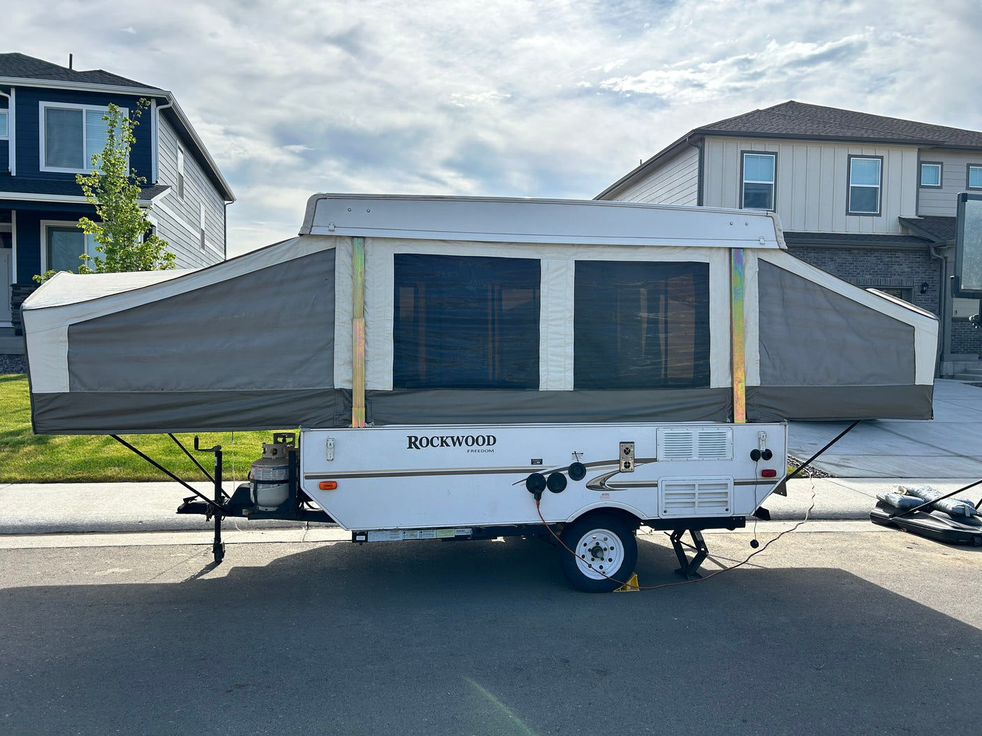 A Rockwood pop-up RV rental, fully set up with canvas sides, is parked on a street. Perfect for camping adventures.