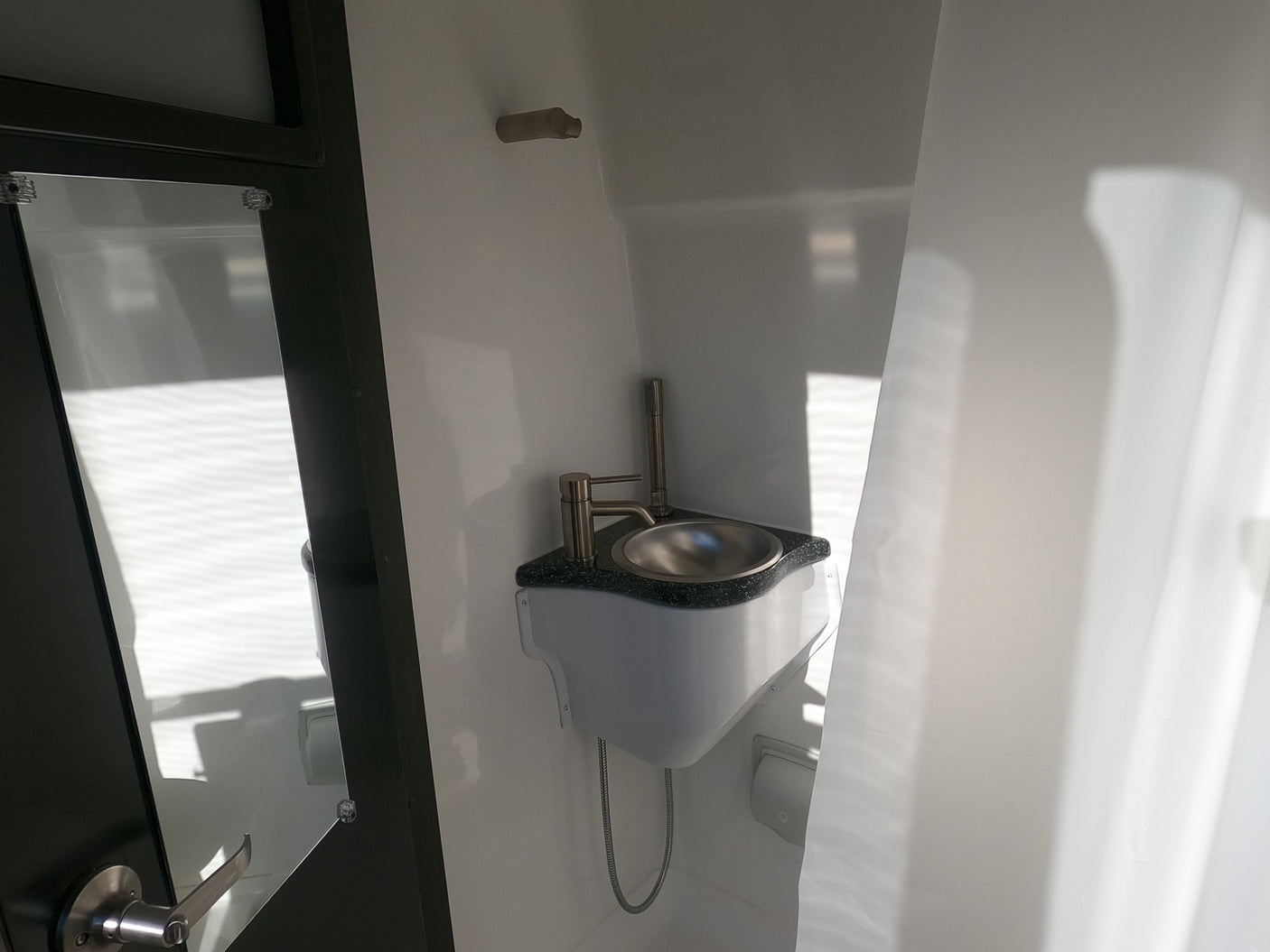 Compact RV rental bathroom: a small, shiny sink with modern faucet, next to a dark-framed door.
