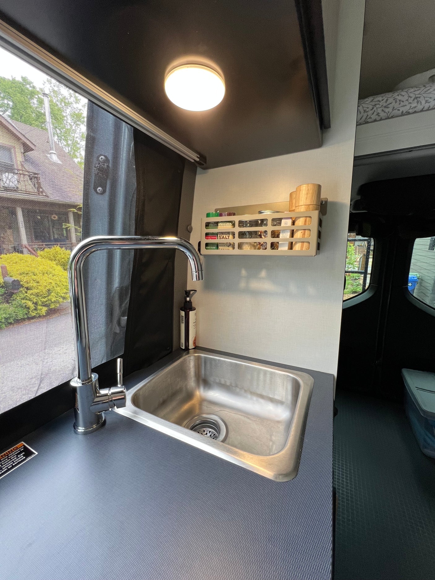 This RV rental features a practical kitchenette with a stainless steel sink, chrome faucet, and a wall-mounted spice rack.