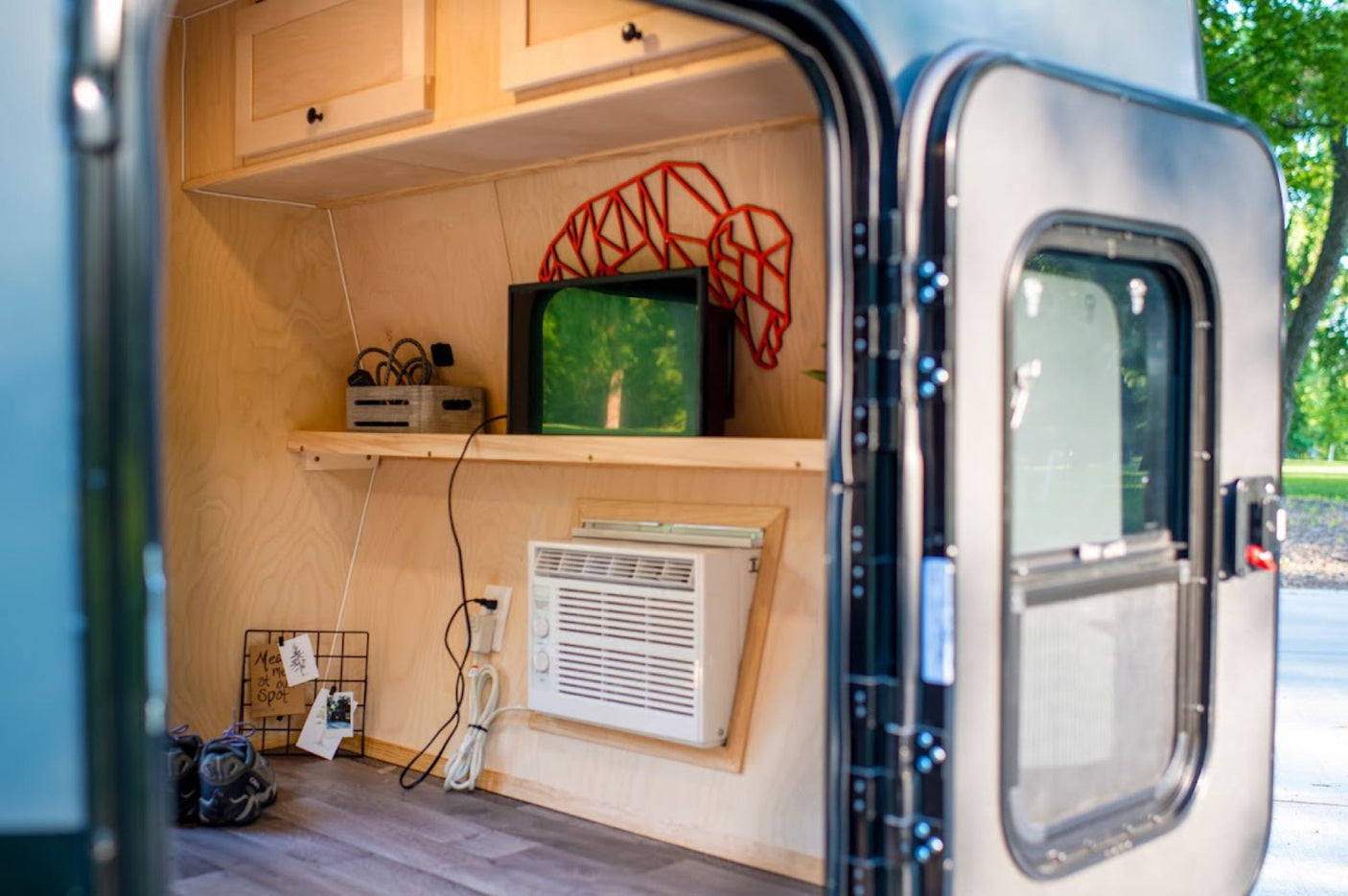 set outdoors.|Woman relaxes reading in a compact grey RV rental trailer. Outdoor setup with laptop & blanket in sunny nature.|Close-up of a compact RV rental camper parked on grass