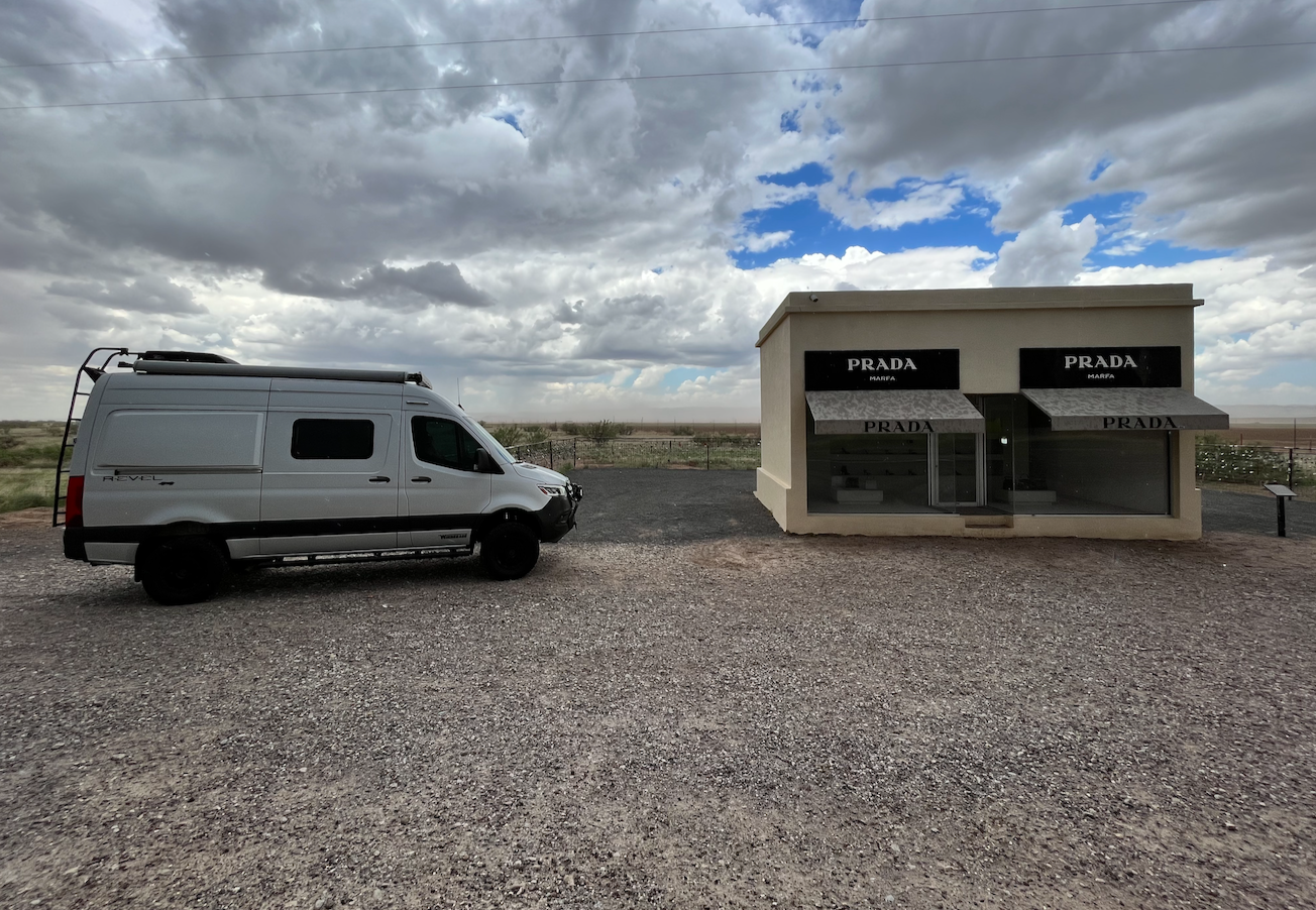 This RV rental (Winnebago Revel) is parked at Prada Marfa, a unique art installation in the desert under a cloudy sky.