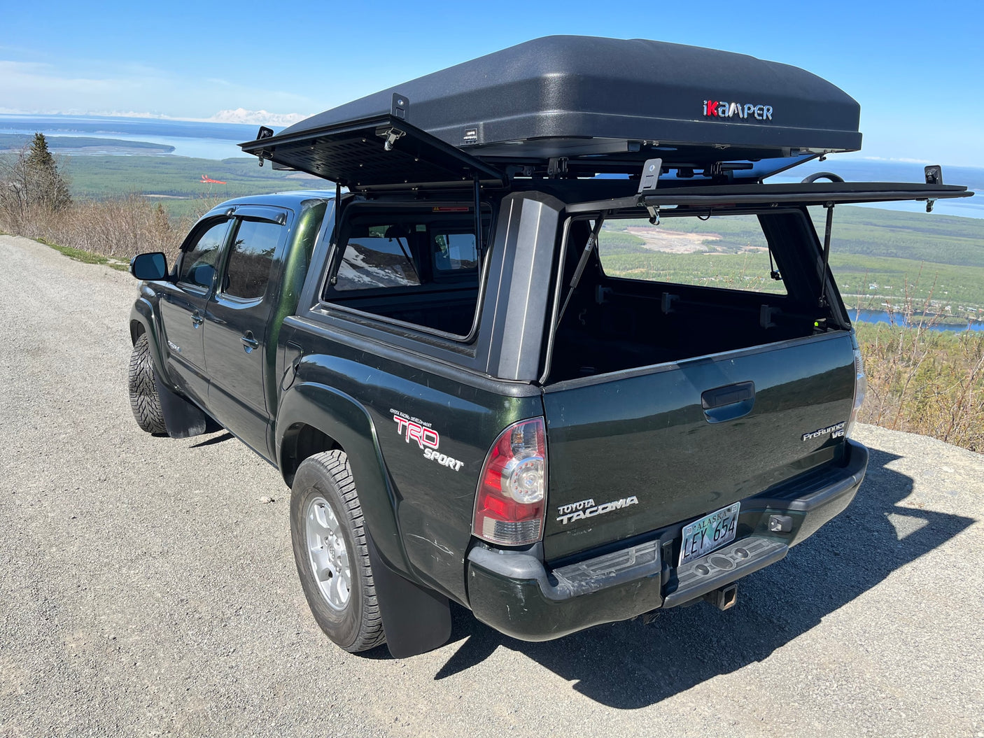 Dark green Toyota Tacoma pickup with an open iKamper rooftop tent, ideal for an RV rental exploring Alaska's scenic views.