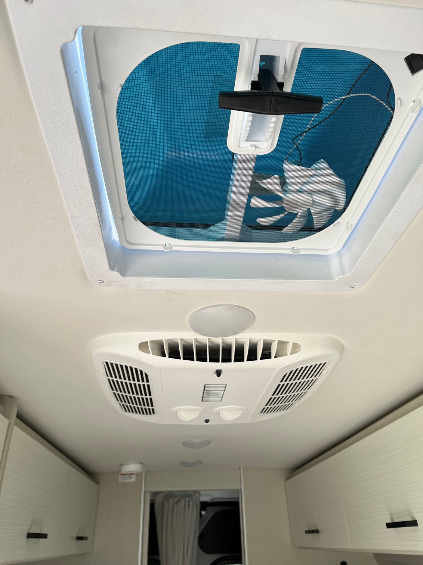 Looking up inside an RV rental: Features a ceiling vent with fan, air conditioning unit, and overhead storage cabinets.